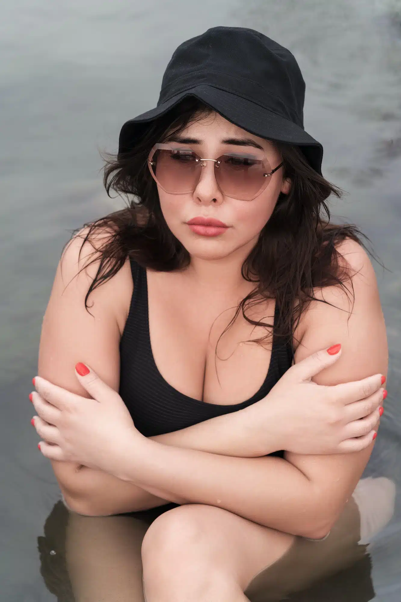 Freezing woman sitting in mineral water in outdoors pool at spa and hugging herself to keep warm